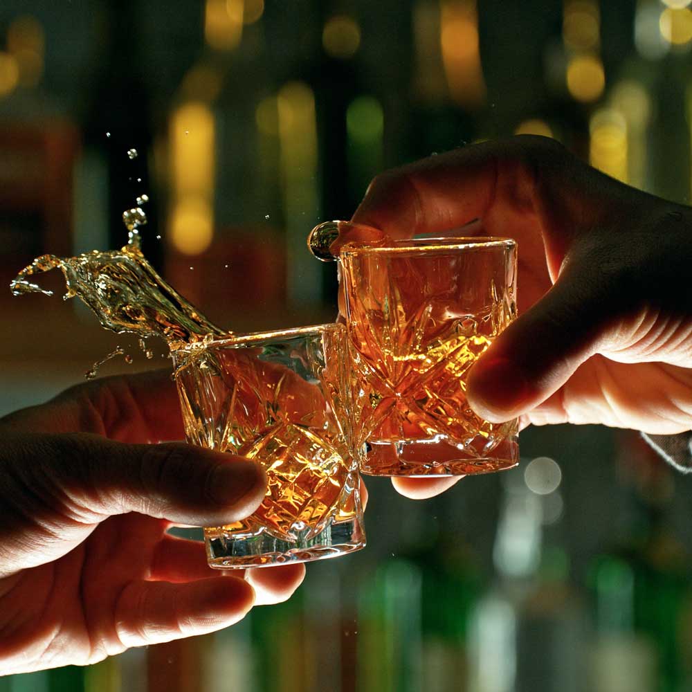 Two hands with two whiskey glasses clinking