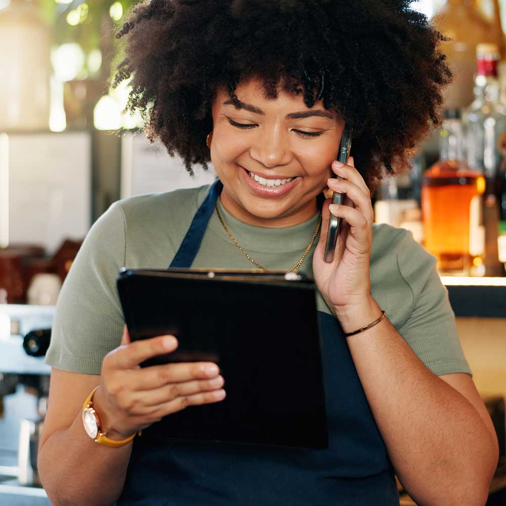 Bartender looking at a tablet and talking on the phone and smiling